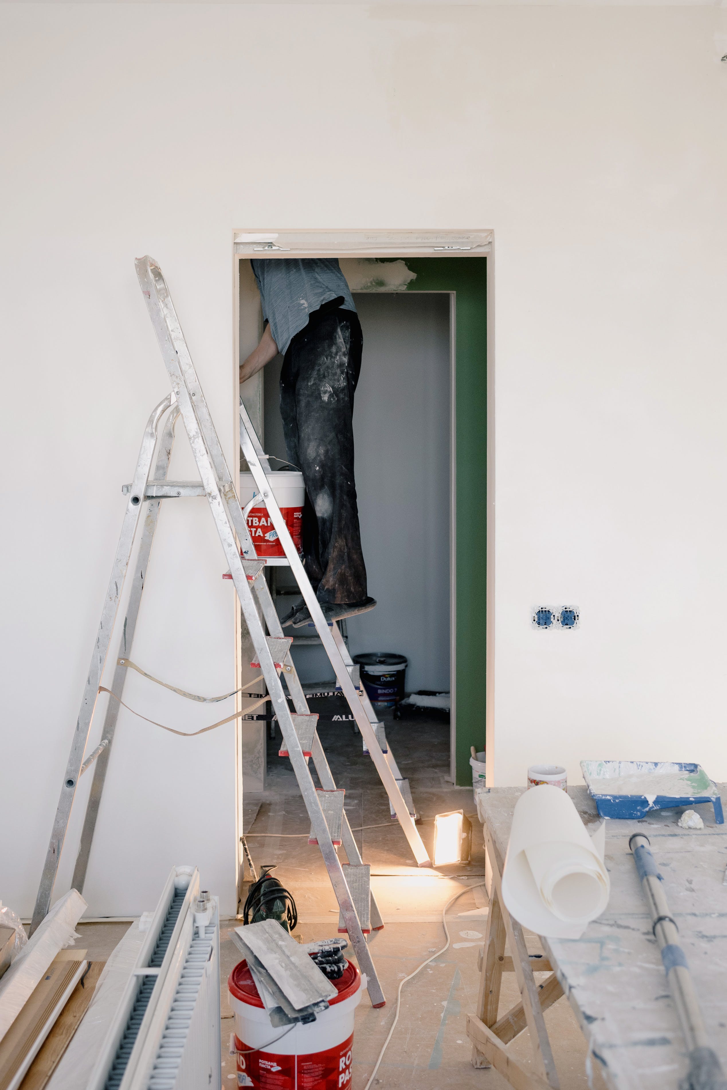 Mann steht auf einer Leiter und malert ein Zimmer.